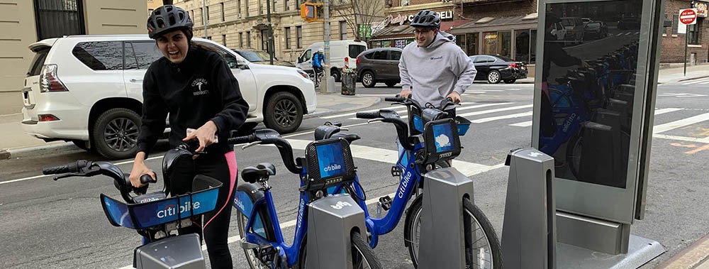 Two people with Citi Bikes returning them to the dock on a street in Washington Heights