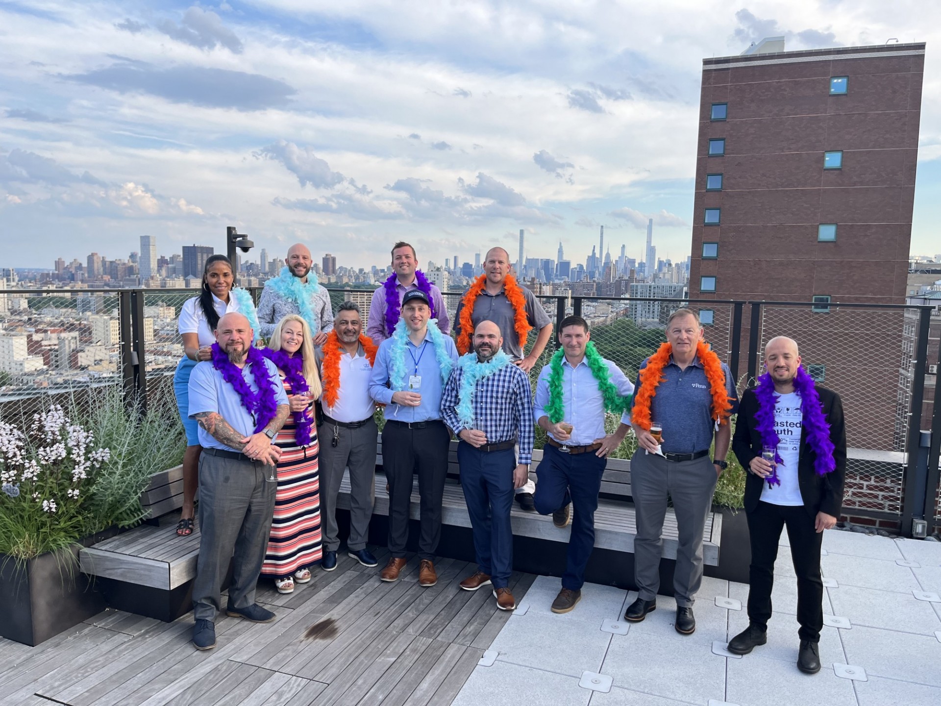 The conference attendees wear colorful leis around their necks while posing on a rooftop, Manhattan in the background