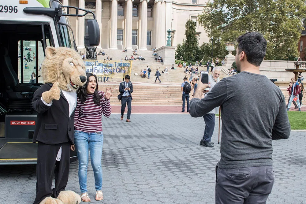 Student poses with Roar-ee in front of electric bus
