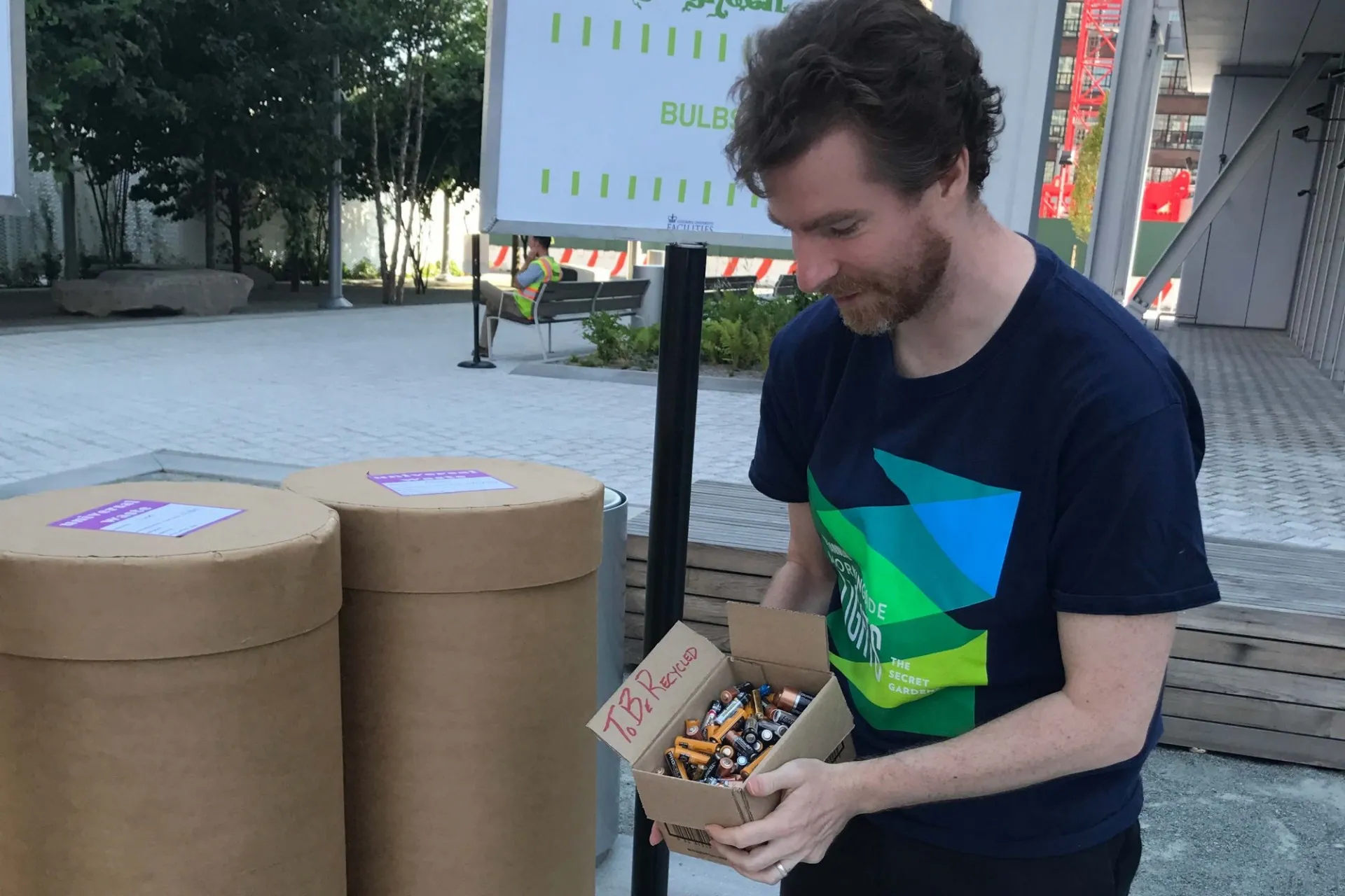 A person holding a box of batteries marked "to be recycled" stands in front of the battery recycling station at the Manhattanville Clean + Go Green event
