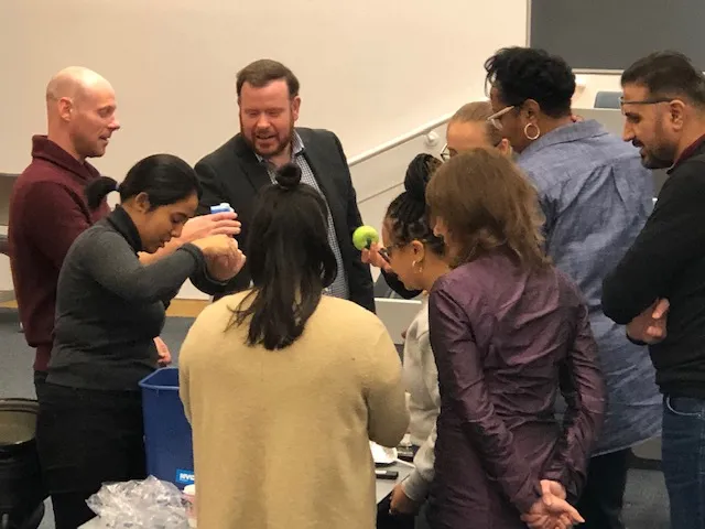 A group of conference attendees surrounds a table in a lecture hall
