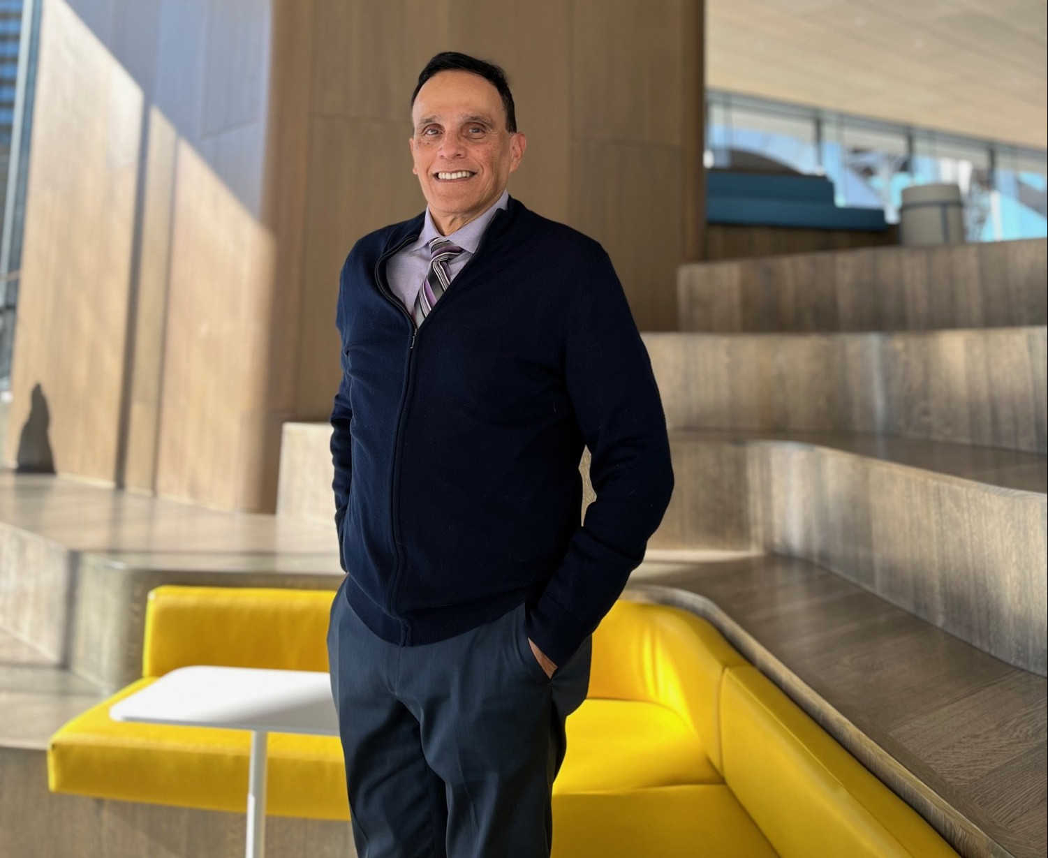 Jim Sugaste stands in an architectural building in front of a yellow couch